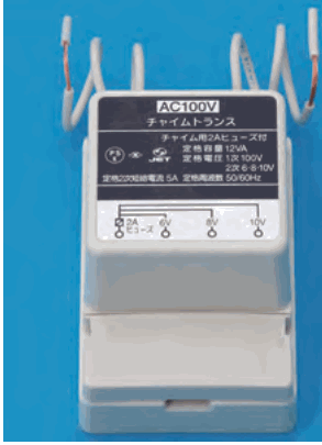 灰白色の器具。上部から白い電線が出ており、銘板に AC100V、チャイムトランス、チャイム用2Aヒューズ付、定格容量 12VA、定格電圧 1次 100V 2次 6-8-10V などの字、端子に 2A ヒューズ、6V、8V、10V の字がある