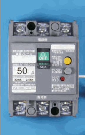 灰色の器具で上下に3つずつ端子ねじがある。上に 電源側、下に 負荷側 の字があり、中央に OFF の字の緑のハンドルと 50A の字、左の表示に 漏電ブレーカ、AC100/200V、50 A、30mA、2.5kA の字、右に黄色のボタン、テストボタン の字の灰色のボタン、トリップボタン の字の赤いボタンがある