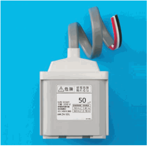 青い背景に置かれた灰色の箱形の機器で、上から灰色の太い管が出て、その先から白・赤・黒の3本の線が出ている。正面のラベルに 危険 感電危険 触れるな、50 μF、三相 200V、50Hz 1.81A、60Hz 2.18A、ZA-50L などの字がある
