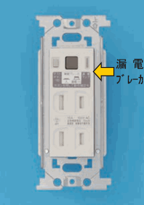 取付枠に付いた白い器具で、上部に黒い四角のボタンなどがあり、黄色の矢印と 漏電ブレーカ の字が添えられ、下部に縦長の刃受が2つずつ上下に2組ある