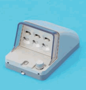 青い背景に置かれた灰白色の器具で,透明なふたの奥に差込口が3つ横に並び,下部に丸いつまみとねじがある