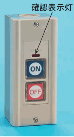 灰色の縦長の箱形の器具で，前面に ON の字の青いボタンと OFF の字の赤いボタンが上下に並び，その上に小さな赤い窓があり，確認表示灯 の字と矢印がその窓を指している