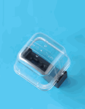 青い背景に置かれた透明な樹脂製のふたで覆われた器具。ふたの中に黒色の部品があり,右下に黒色のつまみ状の部分が出ている
