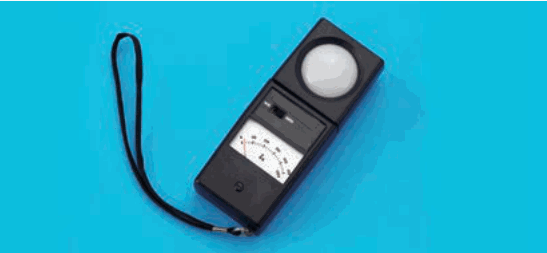 黒色の計器にひもが付いたもの。上部に白い半球形の受光部，下部に指針式の表示板がある