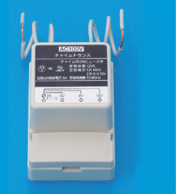 灰色の箱形の器具で,上から白い電線が出ている。正面の表示に AC100V,チャイムトランス,チャイム用2Aヒューズ付,定格容量 12VA,定格電圧 1次 100V 2次 6-8-10V,定格2次短絡電流 5A,定格周波数 50/60Hz,PSEとJETの表示,下部に 2A ヒューズ・6V・8V・10V の端子の図がある