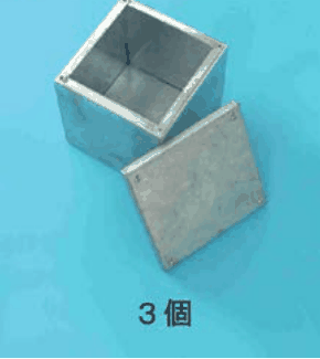 カラー写真。銀色の金属製の深い四角い箱と，横に置かれた四角いふた。3個 の字