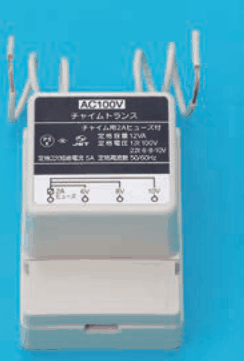 白い箱形の器具で，上から白い電線が数本出ている。銘板に AC100V，チャイムトランス，チャイム用2Aヒューズ付，定格容量 12VA，定格電圧 1次 100V 2次 6-8-10V などの字があり，下に端子の並びの図と 6V 8V 10V の小さな字がある
