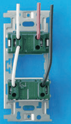 取付枠に上下2つの緑色の器具が付いた裏面。上から来た白線は上の器具の左上の穴へ入り，上の器具の左下の穴と下の器具の左上の穴を白線で渡している。上から来た赤線は上の器具の右上の穴へ入り，上から来た黒線は右側を下って下の器具の右上の穴へ入っている