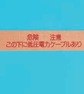 カラー写真。橙色の帯状のシートで,赤い字で 危険 注意 この下に低圧電力ケーブルあり と書かれている