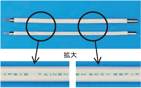白色の平たいケーブル2本で,両端で被覆がはがされている。丸で囲んだ部分が拡大の字とともに下に拡大して示され,表面に緑色の字で <PS>E TAINEN と EM 600V EEF/F の印字がある