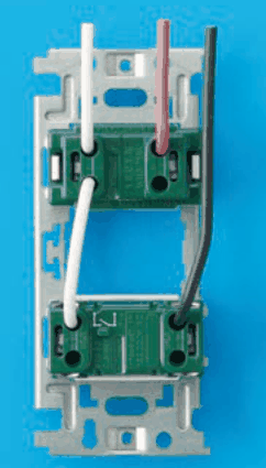 器具の裏面の写真。取付枠に上下2つの緑色の器具が付き，下の器具の表面に記号の刻印がある。上から来た白色の電線が上の器具の左の端子に入り，そこから白色の渡り線が下の器具の左の端子へつながる。上から来た赤色の電線が上の器具の右の端子に入る。上から来た黒色の電線が上の器具を通らずに下の器具の右の端子に入る